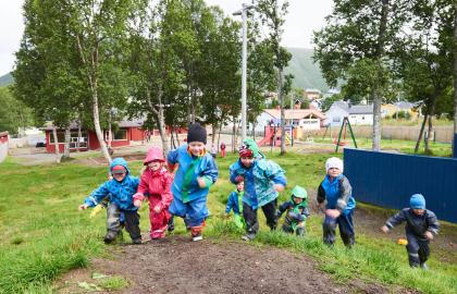 Syv barn som springer opp på en bakketopp i Tromsdalen barnehage en regntung sommerdag