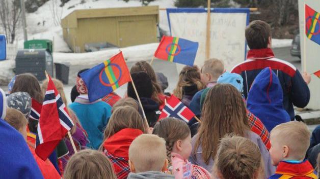 Koftekledde samer går i tog i Tromsø og vifter med det samiske flagget.