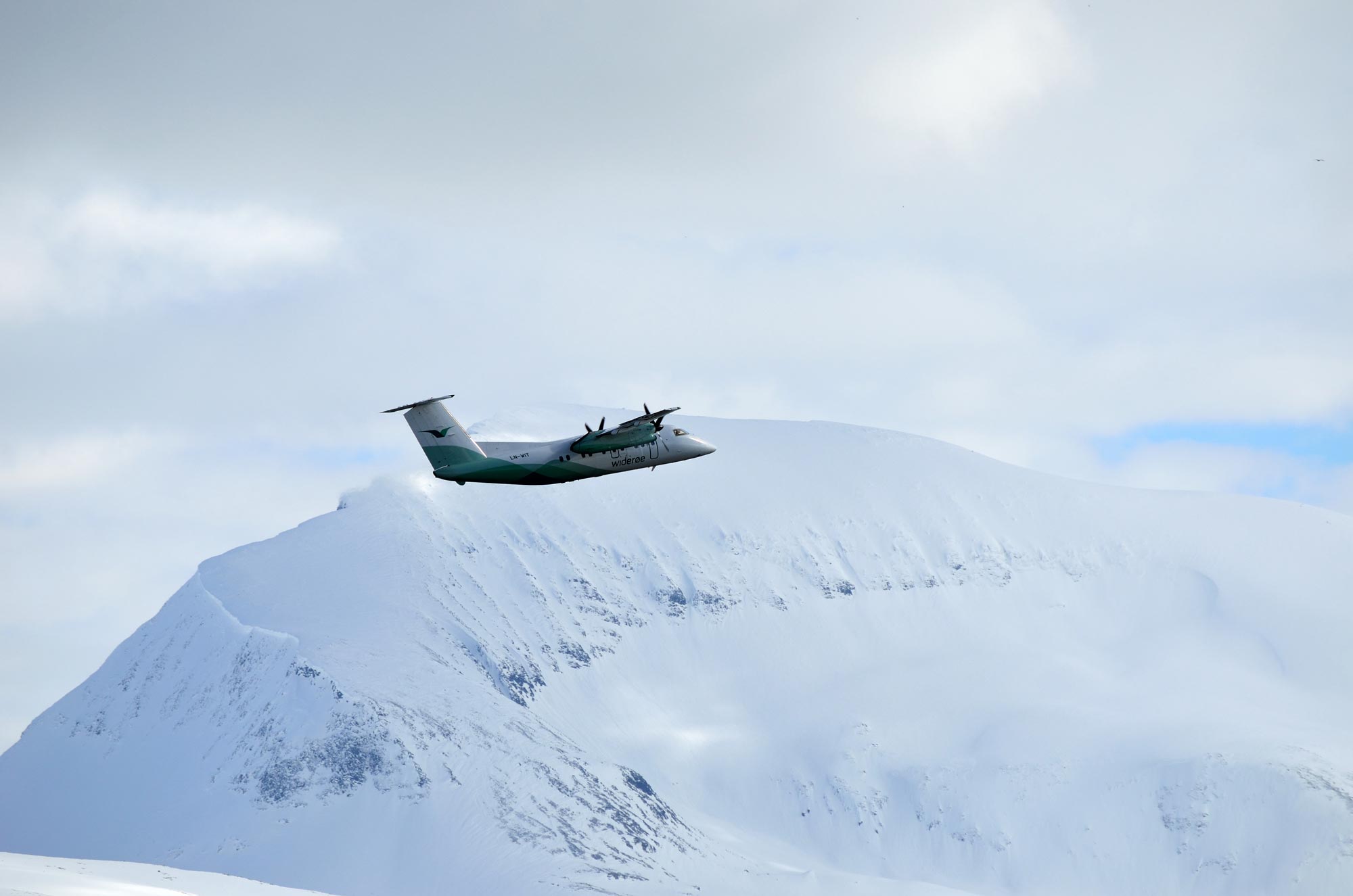 Widerøe-fly i luften over Tromsø med Tromsdalstinden i bakgrunn