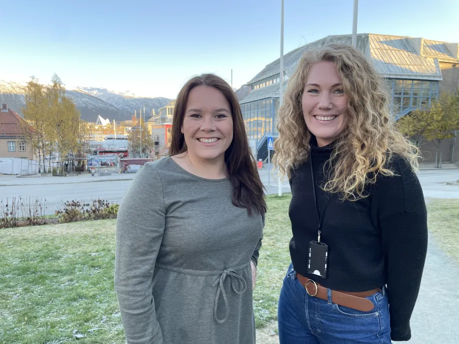 Sigrid Mogård-Jansen, til venstre, og Helga Bårdsdatter Kristiansen fra Tromsø kommune står på plenen utenfor rådhuset, og smiler mot kamera.