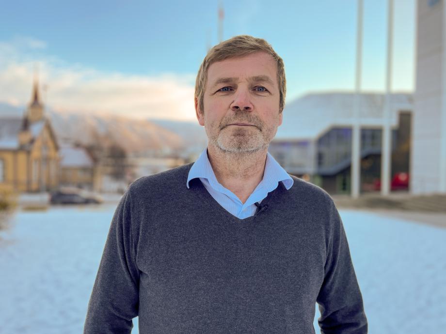 Direktør for stab og finans, Geir Andersen, står på plenen utenfor rådhuset med Tromsø sentrum i bakgrunnen. Snø på bakken.