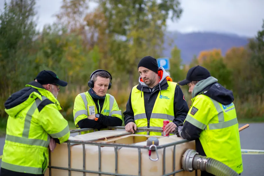 Fire arbeidere står ved vannstasjon i vei