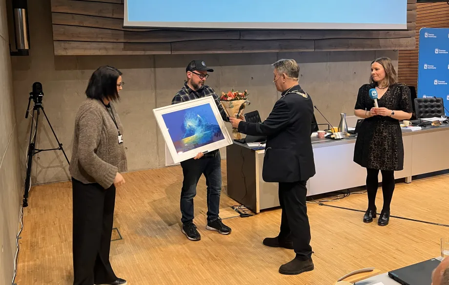 Ed Sivertsen st&aring;r med kunstverk i h&aring;nda. Ordf&oslash;reren overrekker han blomster.