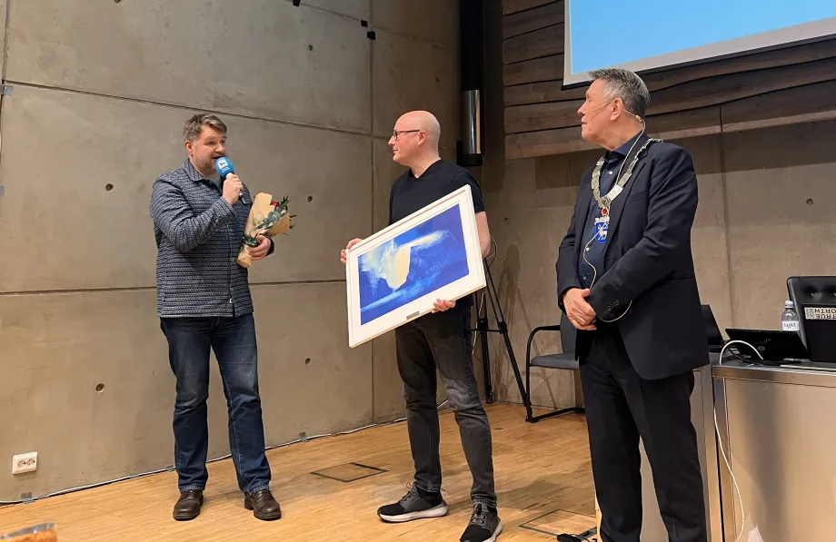 To medlemmer i Troms&oslash; Storband st&aring;r ved siden av ordf&oslash;reren. Det ene bandmedlemmet holder mikrofon mot munnen. Kollegaen holder kunstverk.