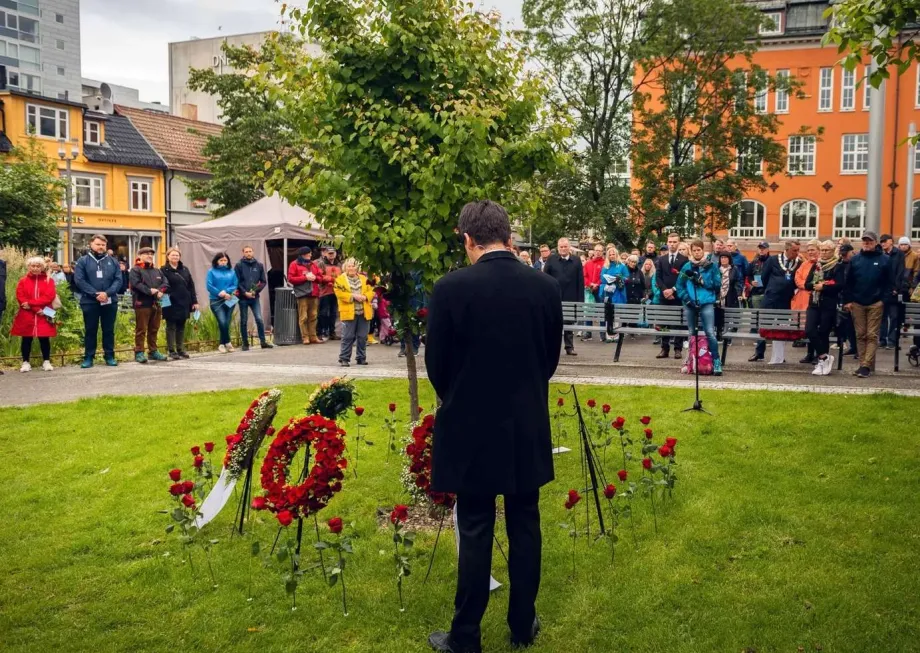 Fra minnemarkering i Domkirkeparken i Tromsø for 22. juli 2011. Mann står med ryggen mot kamera med foldede hender. Bortenfor et knippe publikum ser på.