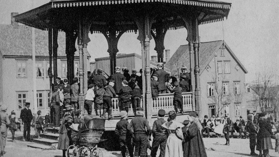 Bildet er tatt en sommerdag i 1902 da Tromsø Totalavholdsforenings orkester ("Totalen") avholdt en søndagskonsert i Rådhusparken. Barna samler seg rundt paviljongen, mens de voksne holder seg lengre nede i parken.