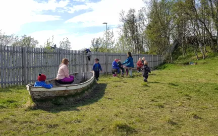 Barn og voksne p&aring; uteomr&aring;det med treb&aring;t, gr&oslash;nt gress og h&oslash;ye tr&aelig;r en solrik sommerdag