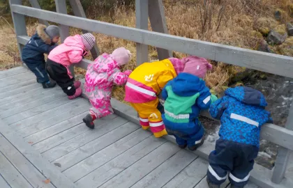 Seks barn som står på en bro og ser ned i elva ved Kattfjord barnehage