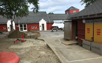 Olsg&aring;rd barnehage uteomr&aring;de med et stort tre, sandkasser og lekeapparater en sommerdag