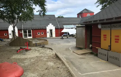 Olsgård barnehage uteområde med et stort tre, sandkasser og lekeapparater en sommerdag