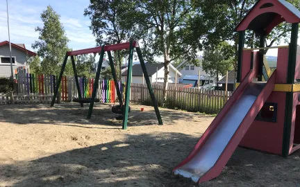 Lekeomr&aring;det i Slettaelva barnehage med h&oslash;ye tr&aelig;r, husker og klatret&aring;rn en solrik sommerdag