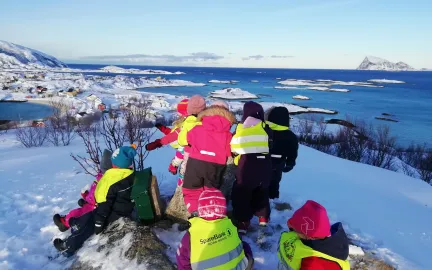 &Aring;tte barnehagebarn fra Sommar&oslash;y barnehage p&aring; tur p&aring; en liten fjelltopp en vinterdag med sn&oslash;, bl&aring; himmel og med utsikt over fjell og hav