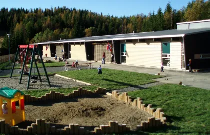 Uteområde i Templarheimen barnehage med grønt gress, husker og sandkasse en solrik sommerdag