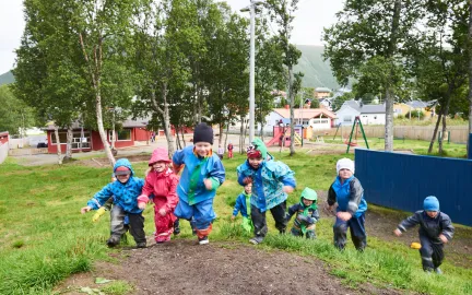 Syv barn som springer opp p&aring; en bakketopp i Tromsdalen barnehage en regntung sommerdag