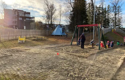 Workinnmarka barnehage uteområde med lavvo, husker og mange barn en solrik sommerdag