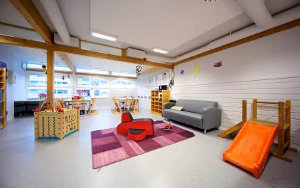 Iinneomr&aring;de med sofa, bord, lekekasser og sklie i Prestvannet studentbarnehage