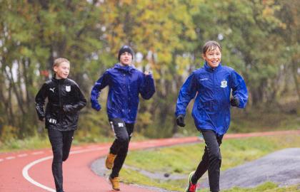 Tre ungdommer løper på treningsbanen på Charlottenlund i Tromsø. Det regner.