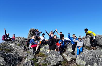 Flere ungdom på sommerleir sittende på en fjelltopp under blå himmel