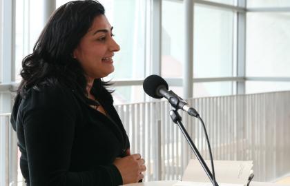 Kvinne med svart hår og svarte klær snakker i en mikrofon. Foto