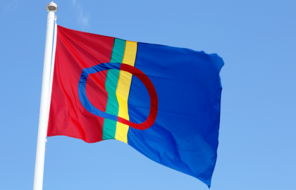 Det samiske flagget på flaggstang mot blå himmel. Foto.