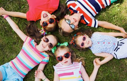 Bilde som viser fem barn med solbriller liggende i gresset