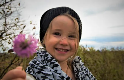 Smilende jente som holder en blomst i hånden