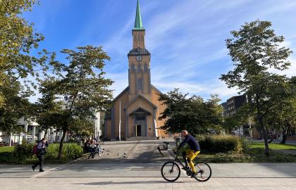 Mann sykler i gaten foran Tromsø domkirke og kirkeparken