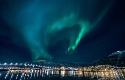 Foto av Tromsøbrua med nordlys på himmelen.