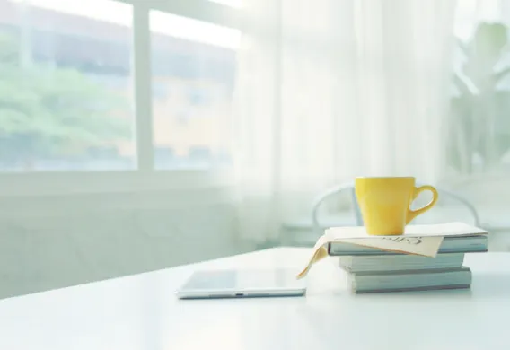 Gul kopp st&aring;r opp&aring; en stabel med b&oslash;ker. Vindu i bakgrunnen. Foto