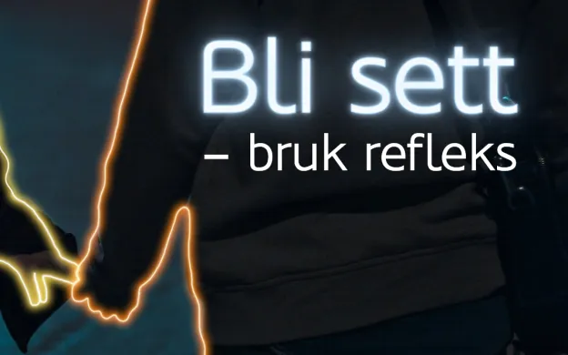 Refleks trafikk To personer som holder hender går langs mørk vei. Tekst i bildet sier: Bli sett - bruk refleks.