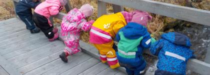 Seks barn som står på en bro og ser ned i elva ved Kattfjord barnehage