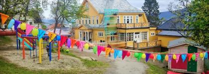 Barnehagen dekorert med hengende fargerike vimpler utenfor barnehagen en sommerdag