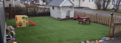 Lekeområdet i hagen med dukkehus, sklie, benk og bord på grønt gress en sommerdag